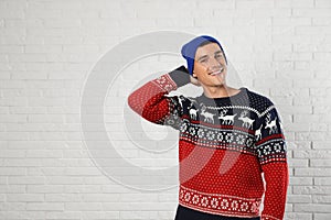 Portrait of young man in  sweater and hat near white brick wall. Space for text