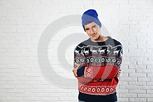 Portrait of young man in Christmas sweater and hat near white brick wall. Space for