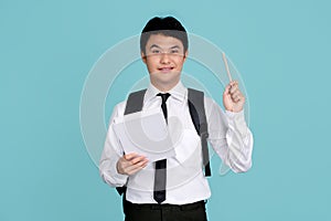 Portrait of young man in college uniform and tie holding notebook and pencil isolated on blue background. concept of thinking