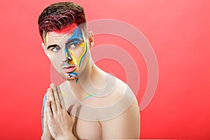 Portrait of young man with colored face paint on red background. Professional Makeup Fashion. fantasy art makeup