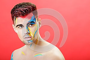 Portrait of young man with colored face paint on red background. Professional Makeup Fashion. fantasy art makeup