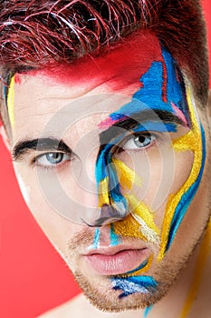 Portrait of young man with colored face paint on red background. Professional Makeup Fashion. fantasy art makeup