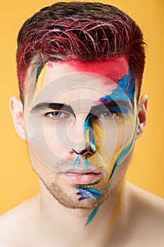 Portrait of young man with colored face paint on yellow background. Professional Makeup Fashion. fantasy art makeup