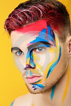 Portrait of young man with colored face paint on yellow background. Professional Makeup Fashion. fantasy art makeup