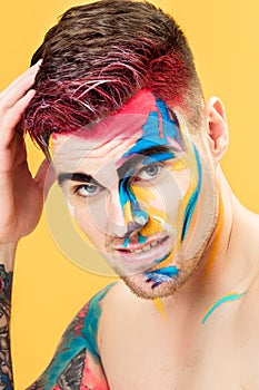 Portrait of young man with colored face paint on yellow background. Professional Makeup Fashion. fantasy art makeup