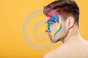 Portrait of young man with colored face paint on yellow background. Professional Makeup Fashion. place for text