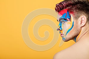 Portrait of young man with colored face paint on yellow background. Professional Makeup Fashion. place for text