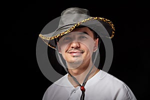 Portrait of a young man in a cowboy hat. Positive guy posing in the studio with black background