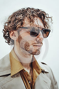 Portrait of a young man with curly hair and bristle posing in a bright studio looking vogue in a close-up