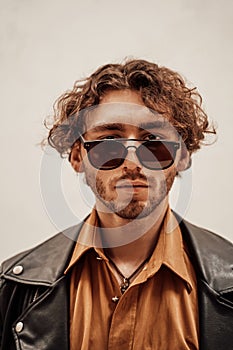 Portrait of a young man with curly hair posing in a bright studio looking self-assured in leather coat