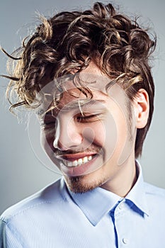 Portrait of young man with curly hairstyle. studio shot. toothy smile and closed eyes