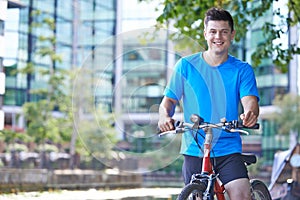 Portrait Of Young Man Cycling Next To River In Urban Setting
