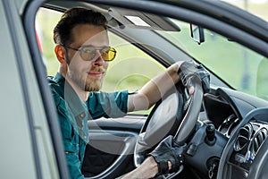 Portrait of a young man in dark glasses driving a car