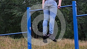 portrait of a young man doing pull-ups on the horizontal bar outdoors on a street playground, a strong athlete
