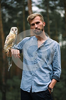 Portrait of young man in forest with owl in hand.