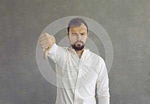 Portrait of a young man giving a thumbs down standing isolated on a grey background