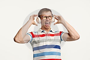 Portrait of young man in glasses posing, listening to music in headphones isolated over white studio background