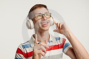 Portrait of young man in glasses posing, listening to online lesson in headphones isolated over white studio background