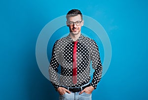 Portrait of a young man with glasses in a studio on a blue background.