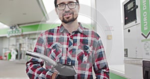 Portrait of a Young Man in Glasses, Stylishly Dressed, Holding a Car Refueling Gun. Shooting At the Gas Station. Fuel