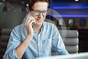 Portrait of a young man with a good mood, a businessman in a shirt and glasses, who works on a laptop and talking on the phone in