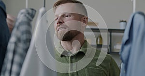 Portrait of young man hanging clean ironed clothes on rails hanger looking at garments smiling