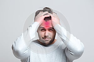 Portrait of young man with headache holding head with hands over white