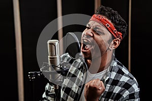 Portrait of young man, hip hop artist looking focused, singing into a condenser microphone while recording a song in a