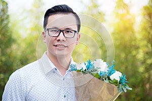 Portrait of young man holding flowers for giving his girlfriend and smiles