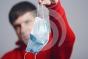 Portrait of young man holding medical protective mask on studio background, boy take off flu mask, concept of personal