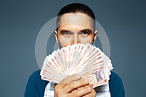 Portrait of young man holding money, Moldovan banknotes, on blue background.