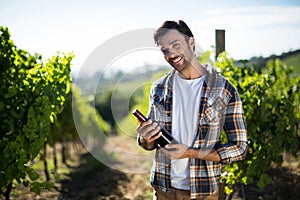 Portrait of young man holding wine bottle at vineyard