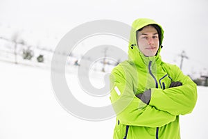 Portrait of young man in hooded jacket standing arms crossed in snow