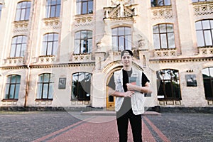 Portrait of a young man with a laptop in his hand standing at a college campus on the background of a building.