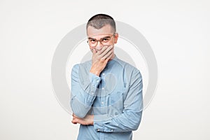 Portrait of young man laughing and covering his mouth with hand over white background.