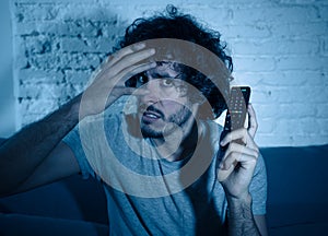 Portrait of a young man looking scared and shocked watching TV. Human expressions and emotions