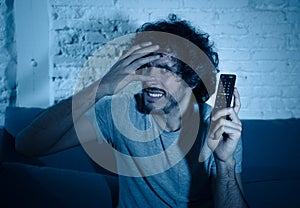 Portrait of a young man looking scared and shocked watching TV. Human expressions and emotions