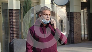 Portrait of young man in lowered medical mask is talking on her smartphoneis. COVID-19 preventive measures. Slow motion