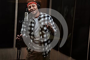 Portrait of young man, male artist looking focused, singing into a condenser microphone while recording a song in a