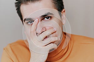 Portrait of a young man. The man covers his face with his hand