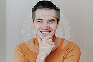 Portrait of a young man. The man puts his hands under his chin and laughs at the camera