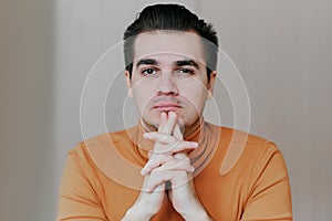 Portrait of a young man. The man puts his hands under his chin and looks at the camera with a sneer