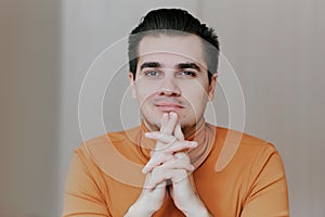 Portrait of a young man. The man puts his hands under his chin and looks at the camera with a sneer