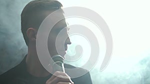 Portrait of a young man with a microphone on a background of smoke in a dark room