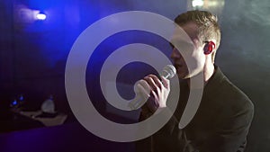 Portrait of a young man with a microphone on a background of smoke in a dark room