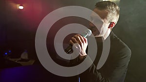 Portrait of a young man with a microphone on a background of smoke in a dark room