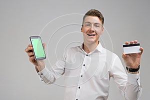 Portrait of young man with mobile phone and Bank card in his hands isolated on white background