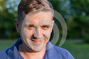 Portrait of a young man on nature background. Emotion facial expression. Smug smile, feelings and people reaction