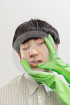 Portrait of young man with piercing posing with hands in rubber gloves on face  over grey studio background