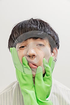 Portrait of young man with piercing posing with hands in rubber gloves on face  over grey studio background